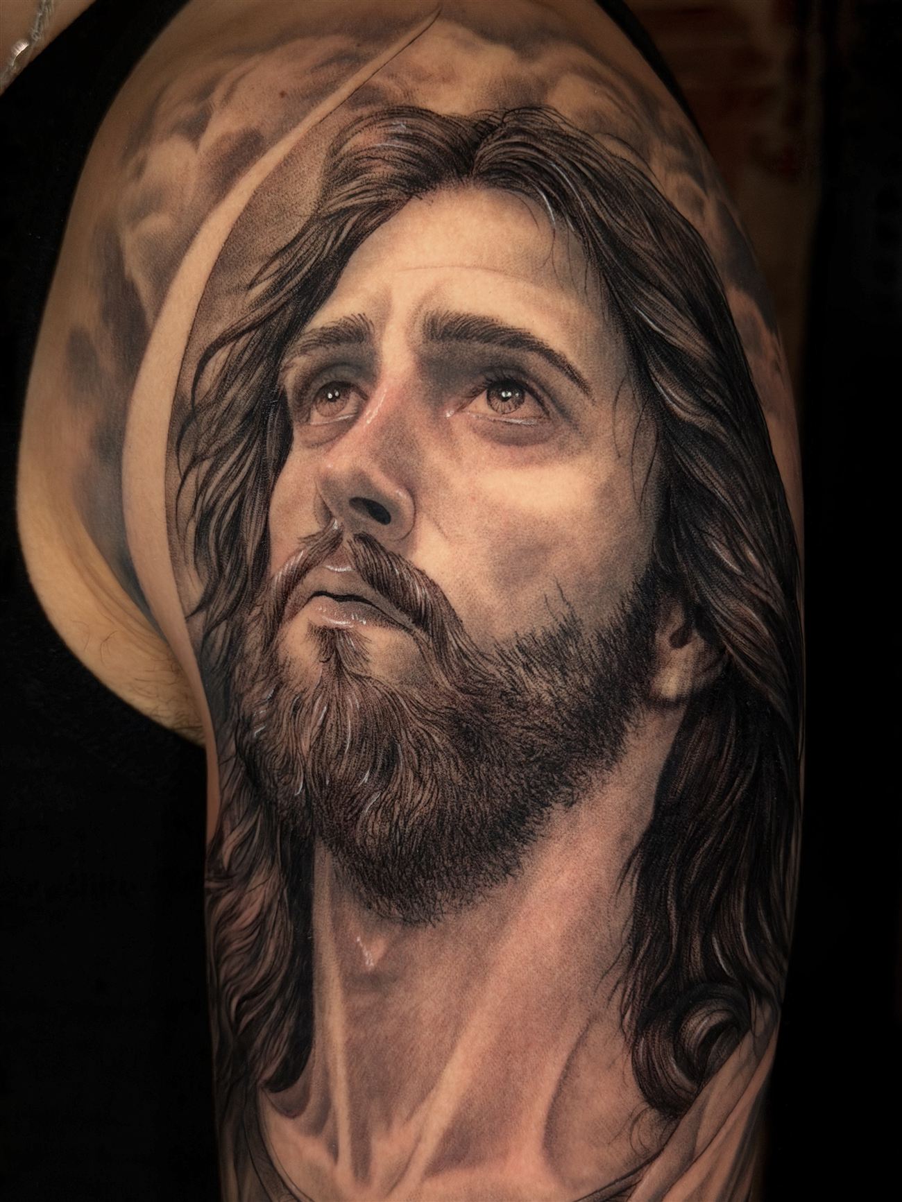 Tatuaje de realismo en blanco y negro de un retrato sacro sobre el hombro