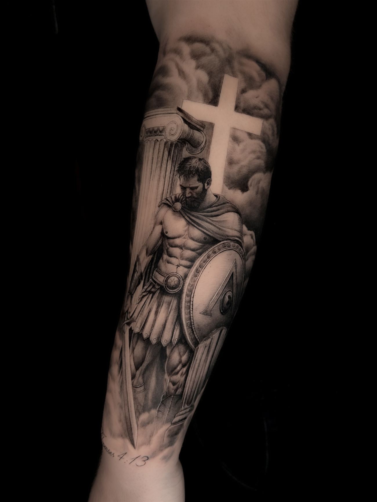 Tatuaje de realismo en blanco y negro de un guerrero clásico junto a una columna jónica y una cruz